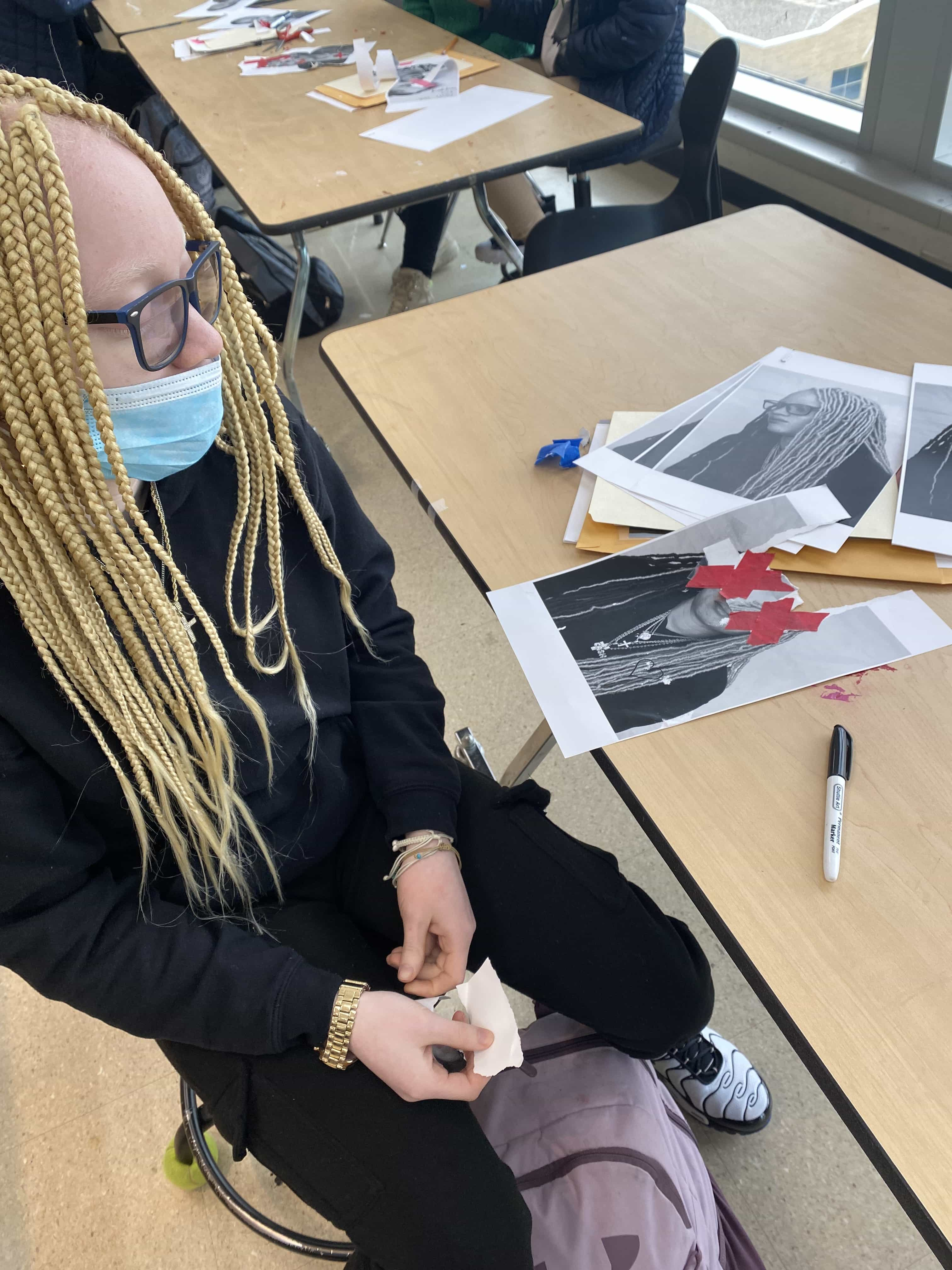 Adult wearing a mask sifts through images and papers spread out on desk.