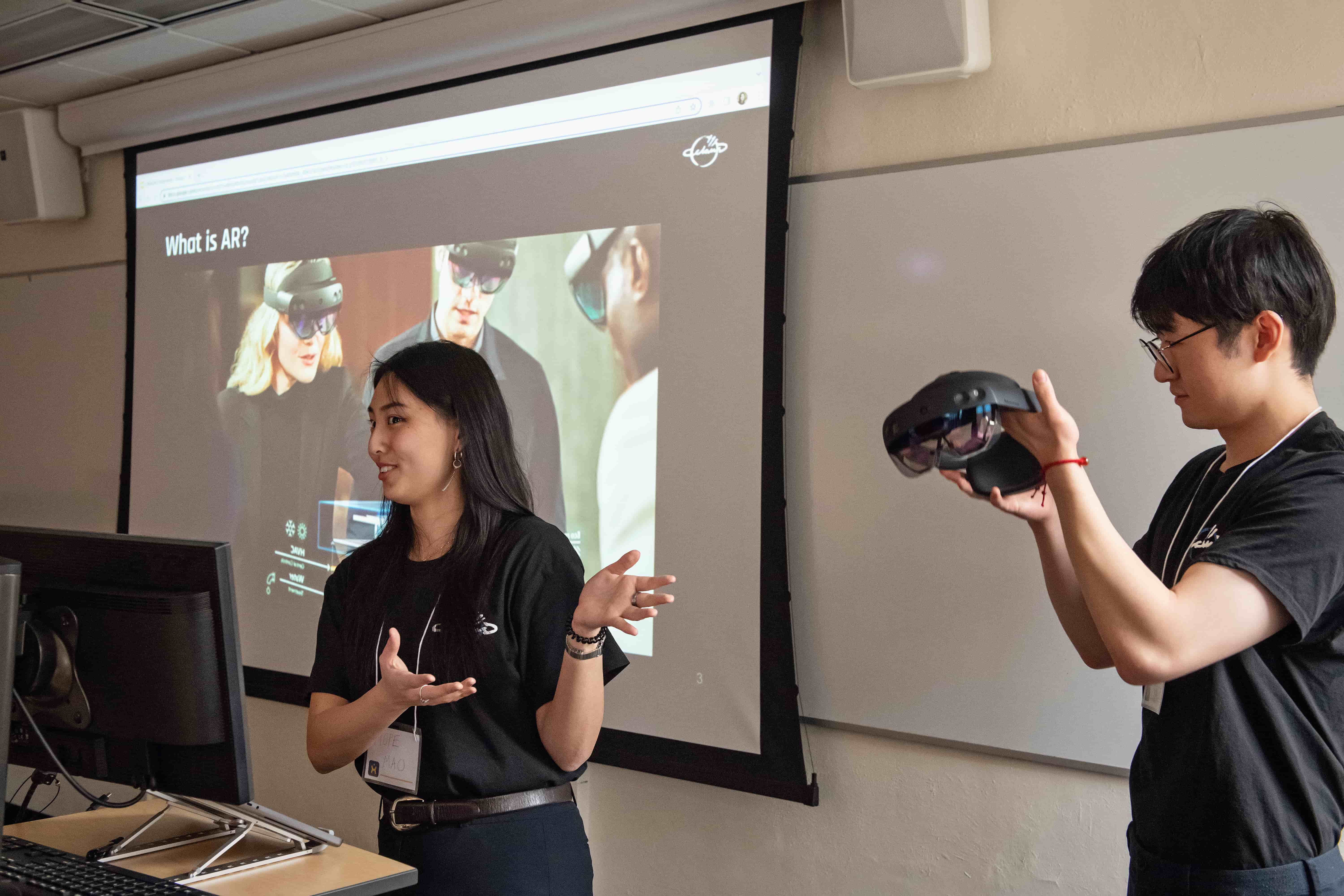 Student presents in front of a classroom as a classmate records.