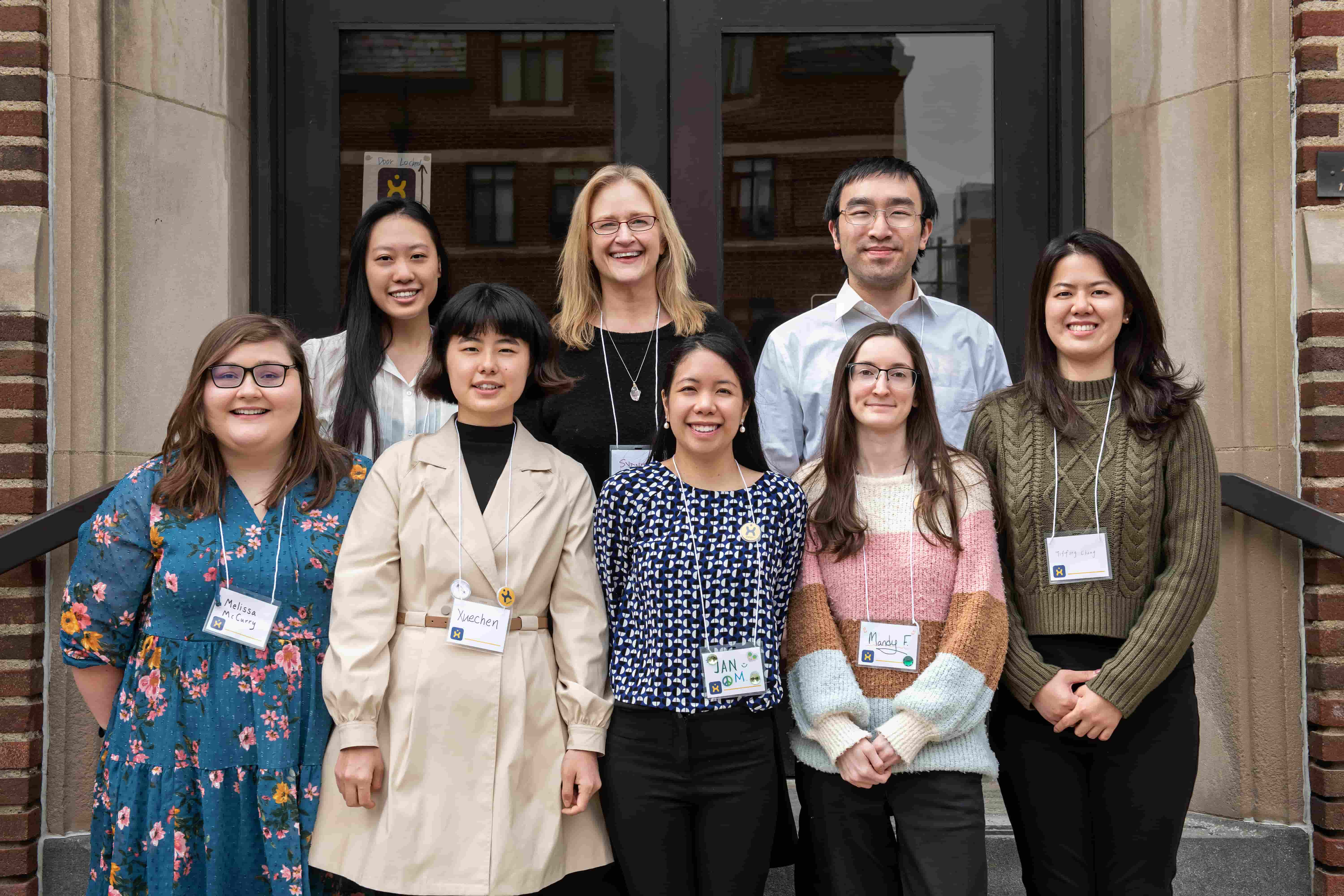 Group of conference organizers wearing name tags pose and smile for photo.