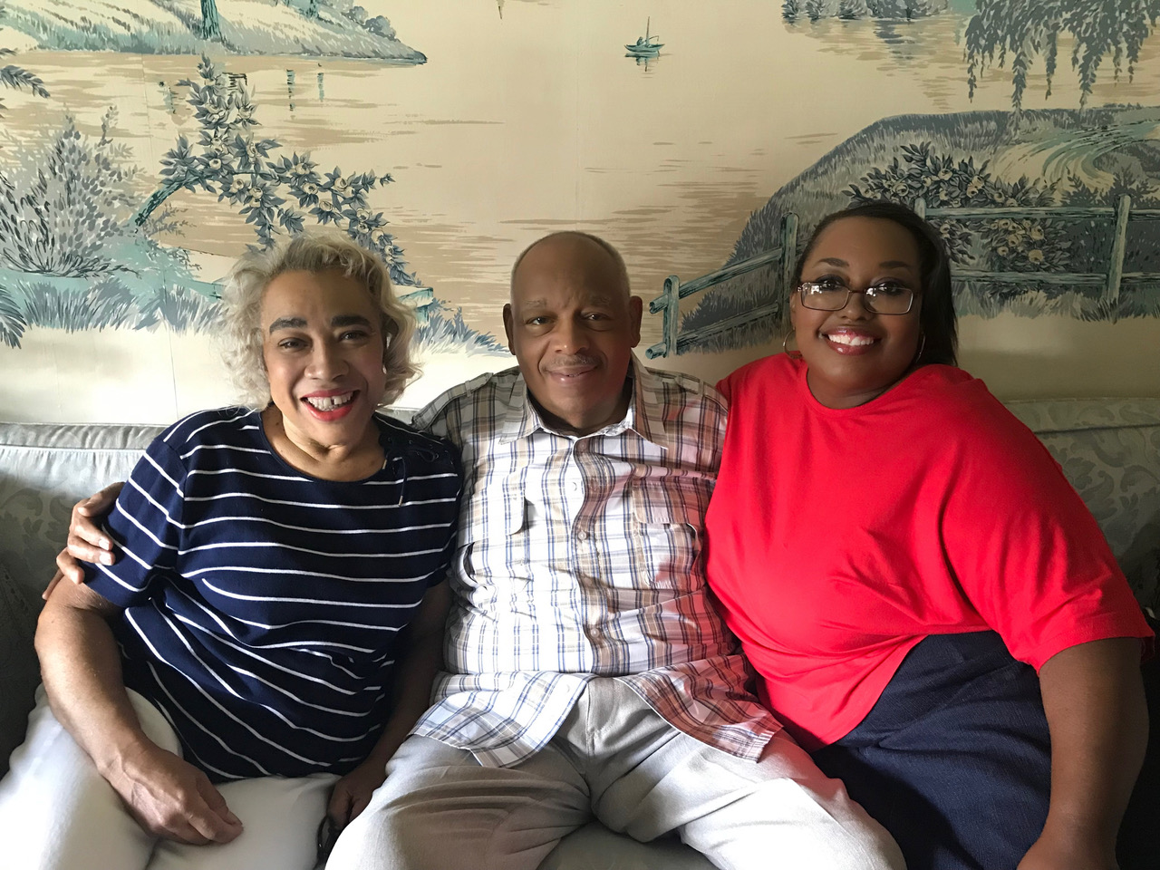 Three smiling adults posing on a couch.
