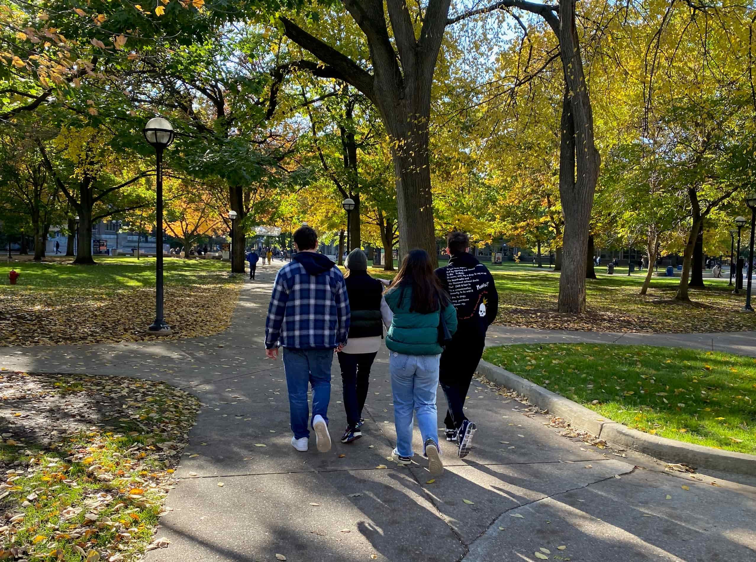 Four adults in fall clothing walk into the diag away from the camera.