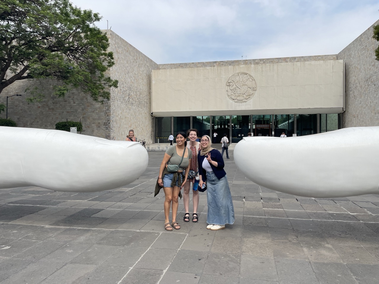 Three ELD interns pose in front of the Mexican Museum of Anthropology in Mexico City. They stand in front of a sculpture of two giant human fingers.