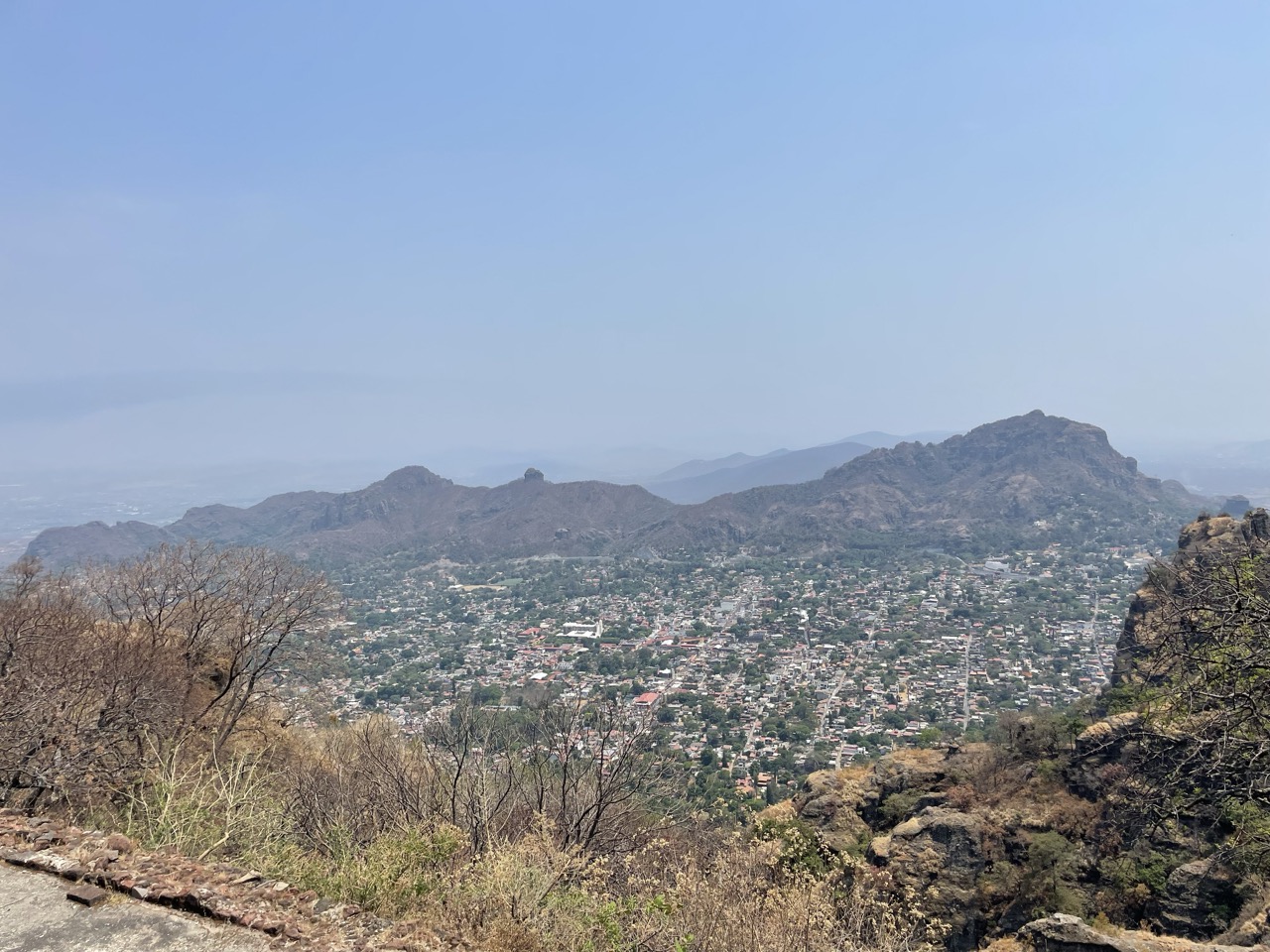 A distant view from the top of the Tepoztlan mountains shows the town below and other mountains in the background.