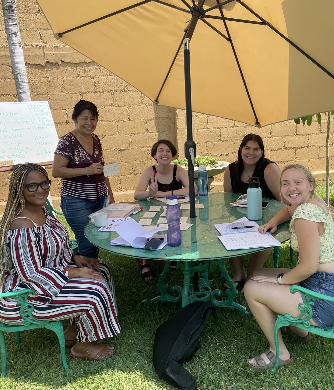 Four interns pose at an outdoor umbrella table with their Spanish teacher during a language lesson.