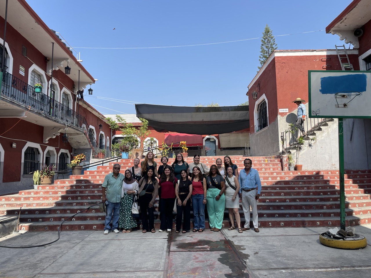 A group of interns stand in front of a large set of red stairs at a Mexican public elementary school during a school-visit.