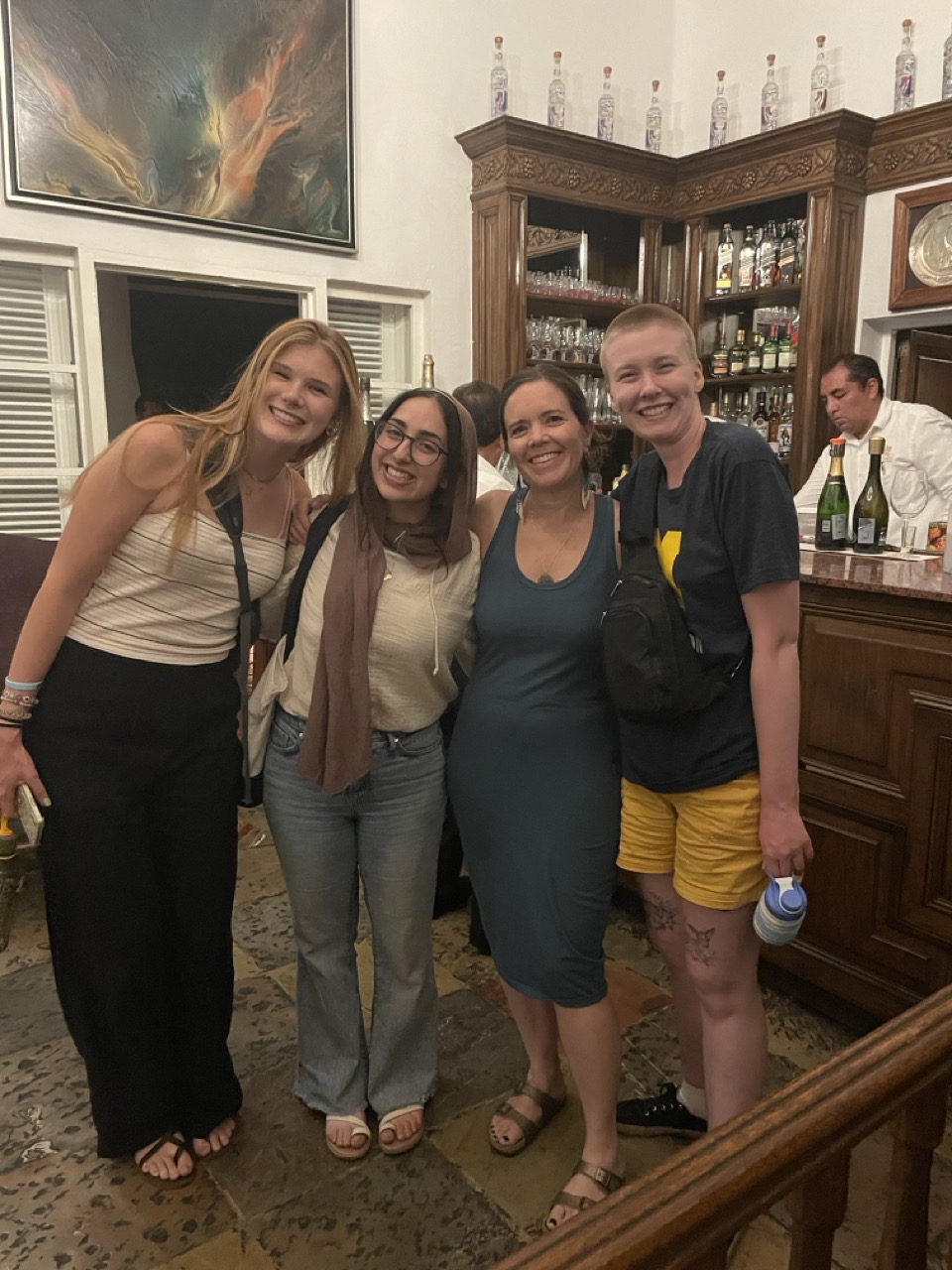 Julia, Nour, Susan and Asa stand in a cluster and smile in front of a wooden bar at Las Mananitas restaurant in Cuernavaca, Mexico.