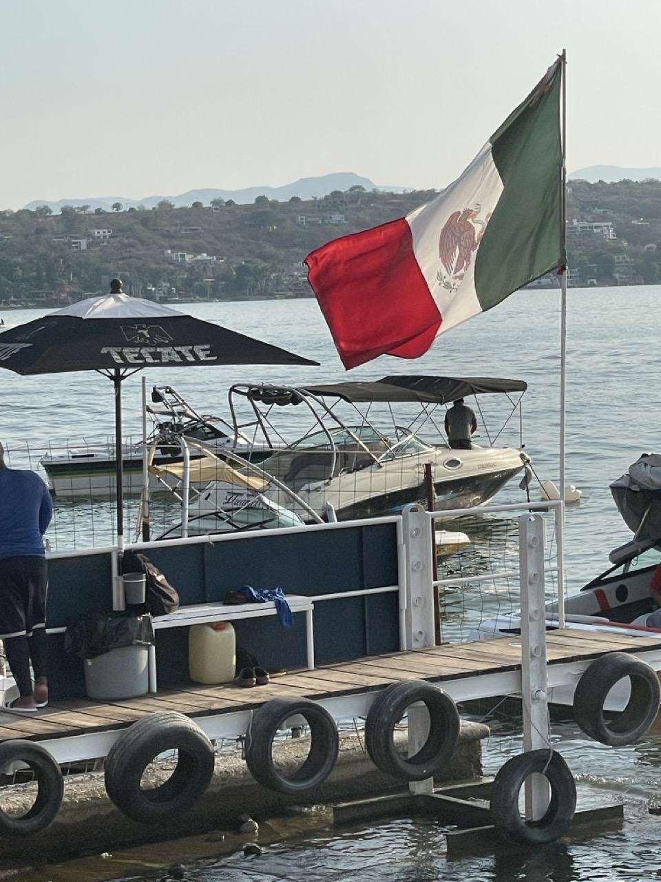 A Mexican flag flutters in the wind in front of some boats and a dock on the bank of Lake Tequesquitengo.