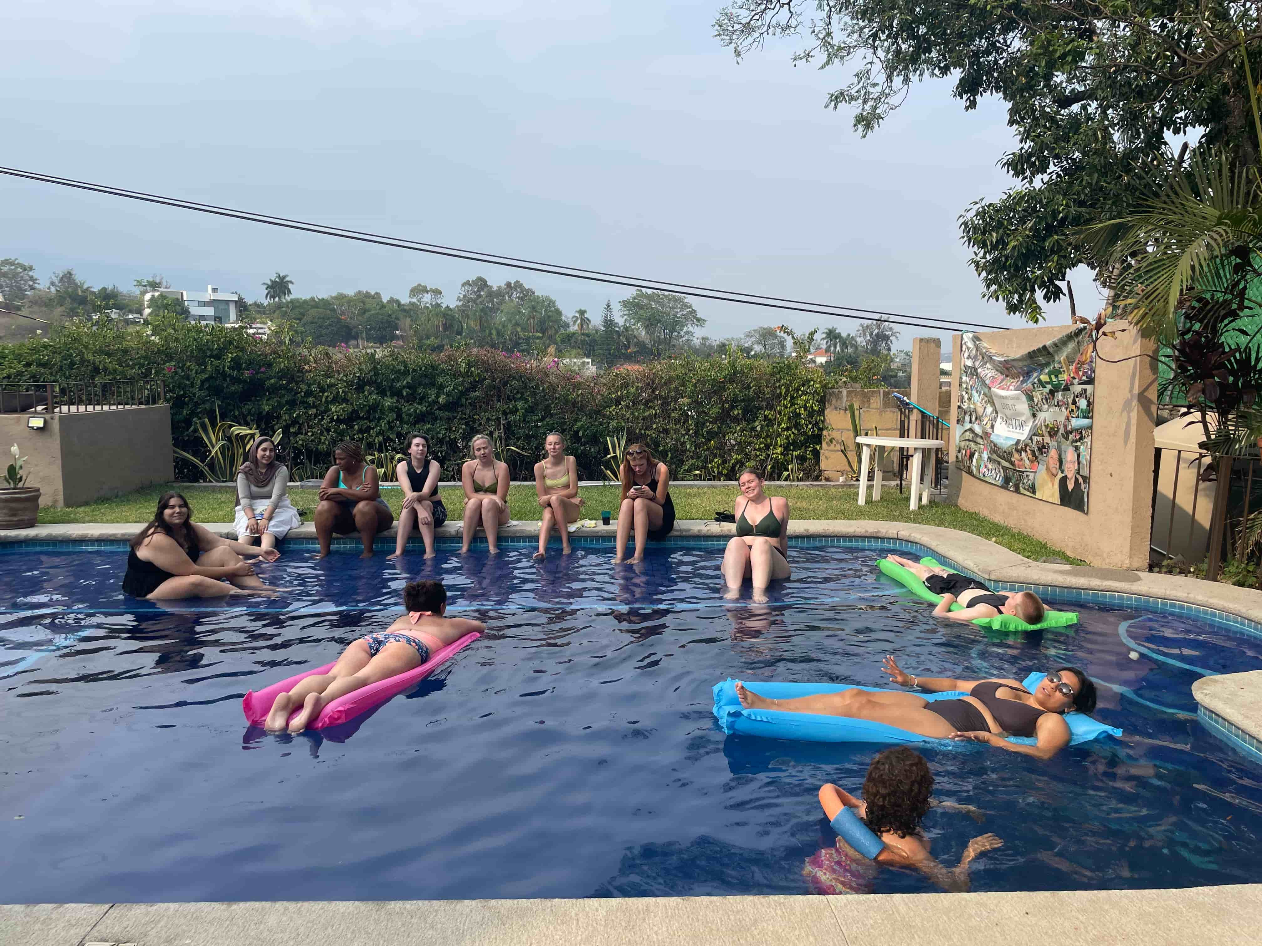 Interns talk and float lazily on inflatables in a pool, while others sit on the edge, enjoying the conversation and cool water.