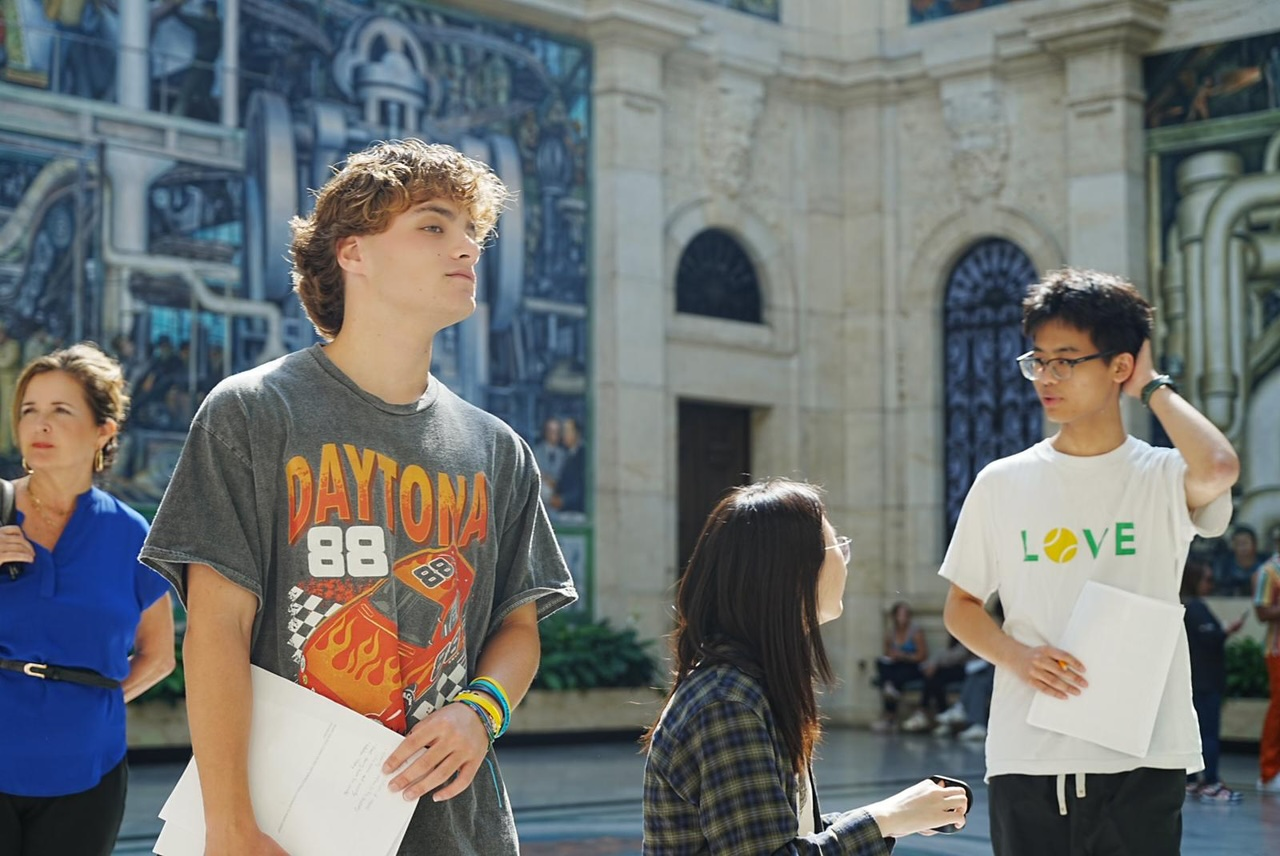 Three LEAPS students discuss and take notes in front of The Detroit Industry Murals by Diego Rivera at the Detroit Institute of Arts