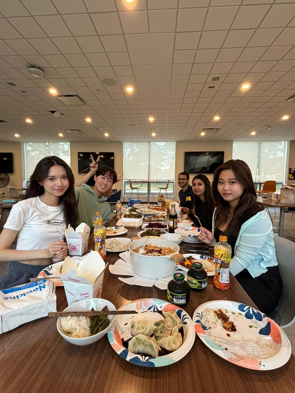 Five students gather on either side of a long table, laden with dumplings and different pots of food to celebrate Mid-Autumn Festival