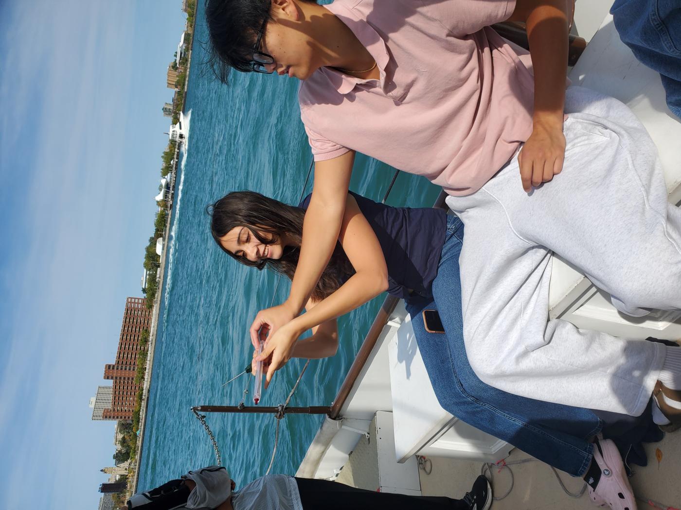 Two students on a boat hold a small device to measure something 