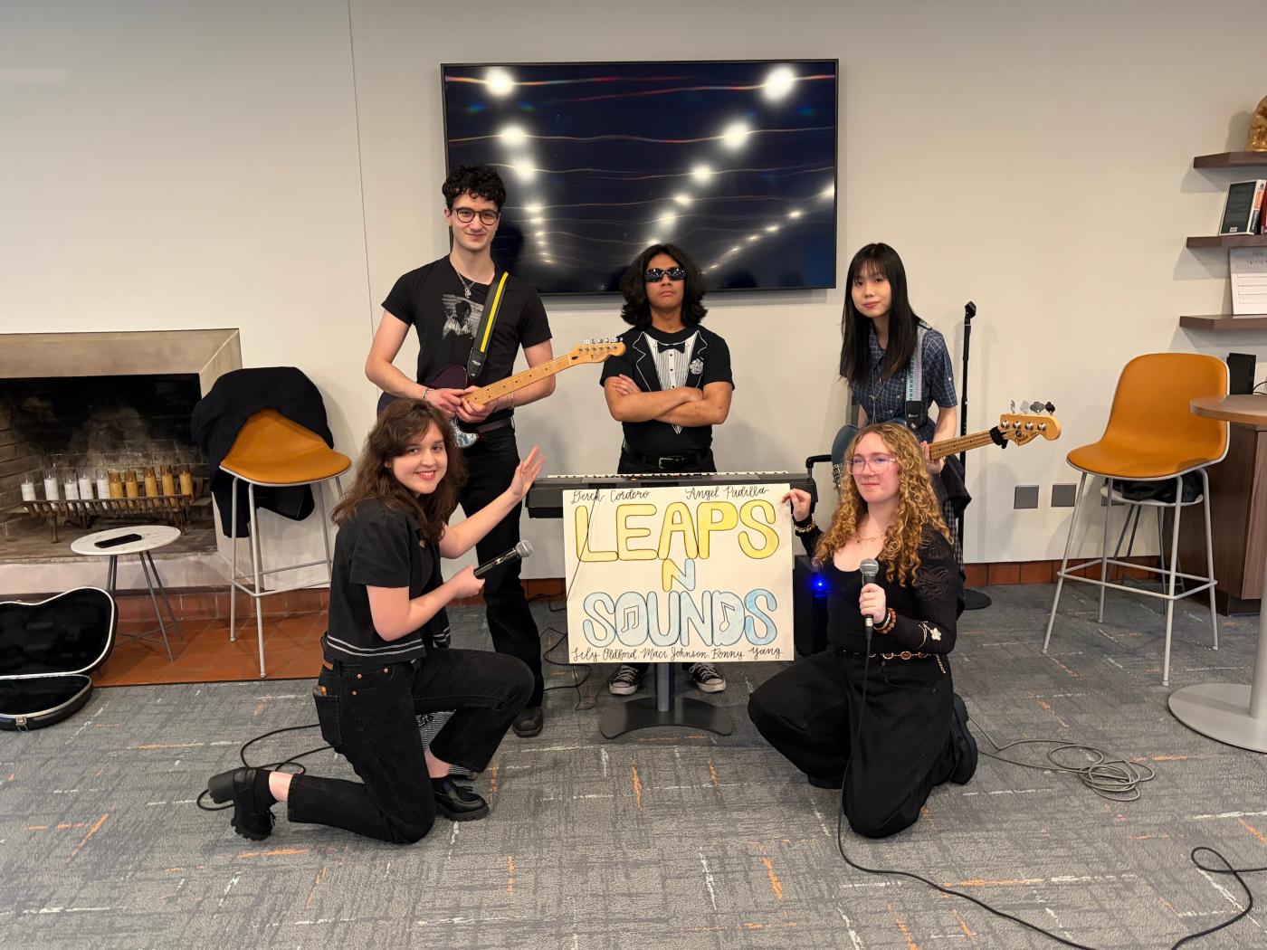 Five students with instruments stand next to a sign that says Leaps N Sounds. 