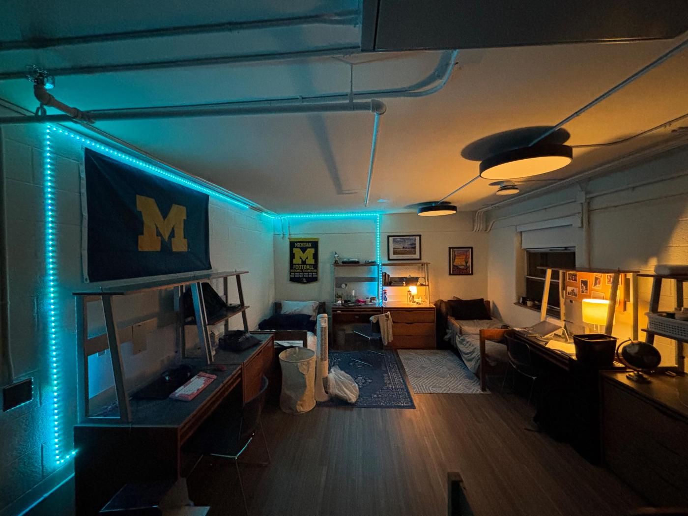 Residence hall room in Florent Gillet. Blue bead lights outline the wall, two beds and two desks fill up the space with small rugs on the floor.