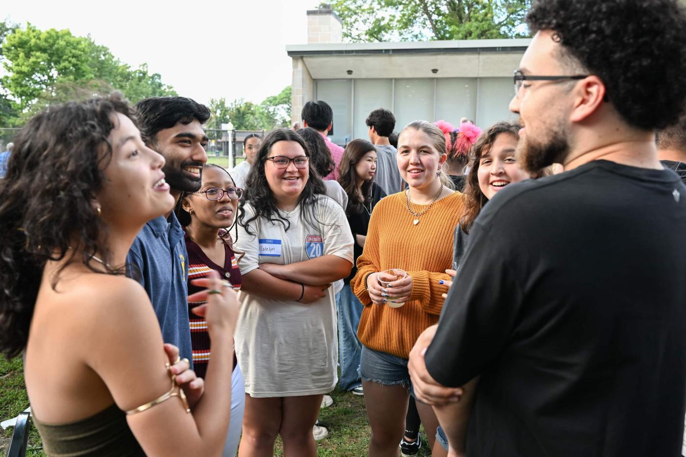 A group of students stand in a circle outside smiling and talking. 