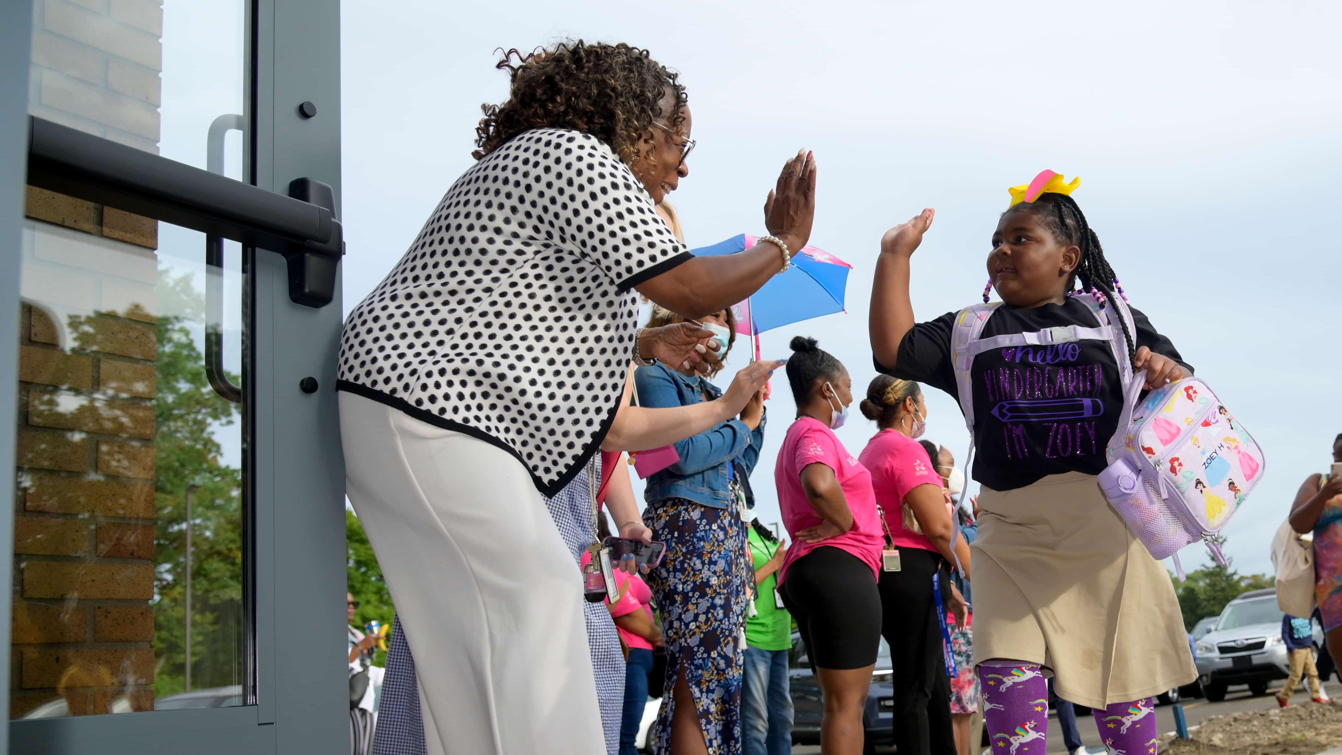 An elementary school administrator gives a child a high five as the student enters the building for her first day of school.