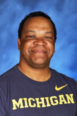 Headshot of Eugene Thompson. Eugene wears a blue shirt with maize Michigan letters and a Nike logo on the chest, stands in front of a blue background, and smiles into the camera.
