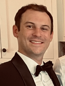 Headshot of adult in a suit with black bowtie, smiling.
