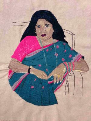 Embroidered portrait of a woman wearing a blue sari, sitting in a chair, holding her hands before her.