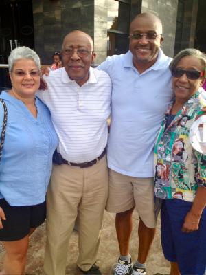 Four people stand together with their arms around each other.