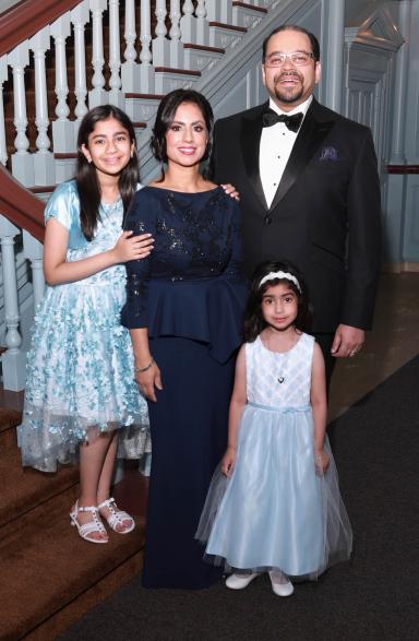 Dr. Ruby Siddiqui and her family, in dress attire, smile and pose for a photo in front of a staircase.