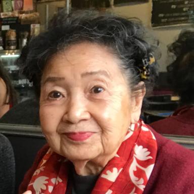 Headshot of senior adult wearing a red scarf, smirking.