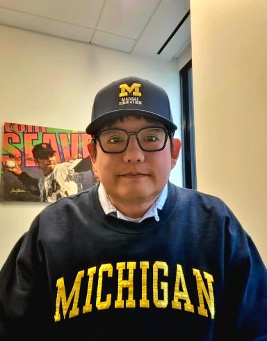 Eric Huang is smiling at the camera, wearing a Michigan hat and sweatshirt