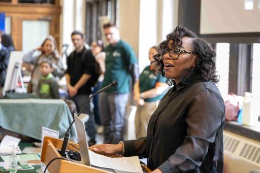 Dr. Natalie Davis delivers remarks at a podium. In the background guests at an event listen to her welcome address.