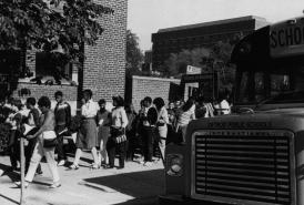 Scan of a black and white photo from 1985 of children from Detroit Public Schools exiting a DPS bus and entering the School of Education building 