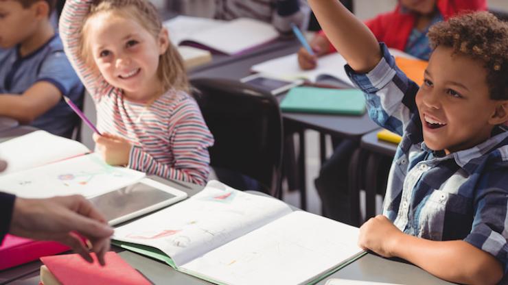 Children in a classroom with hands raised