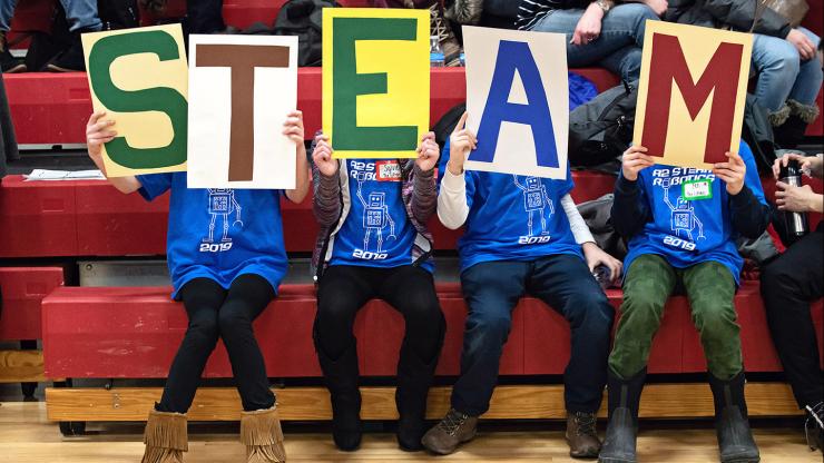 Robotics students hold a sign that spells STEAM