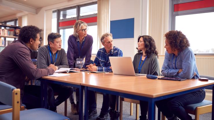 Teacher with group of mature adult students in class sit around table and work in college library