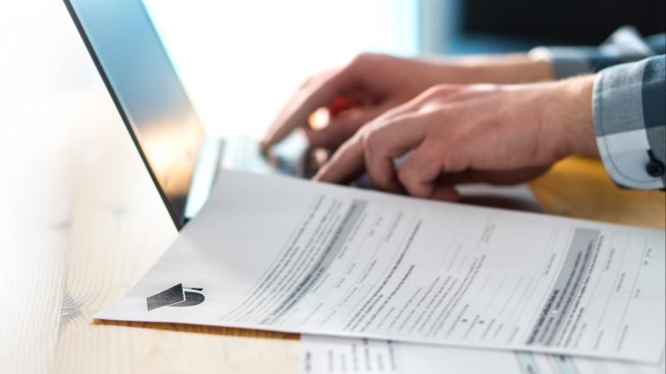 Photo of person's hands typing on laptop, with college admissions papers in the foreground