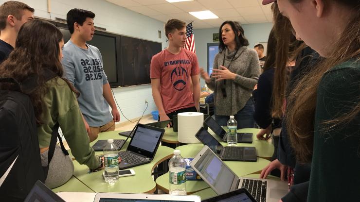 Teacher interacting with students around a table.