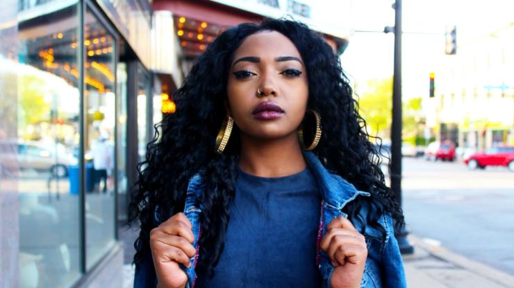 Young Black woman in denim jacket, walking across campus.