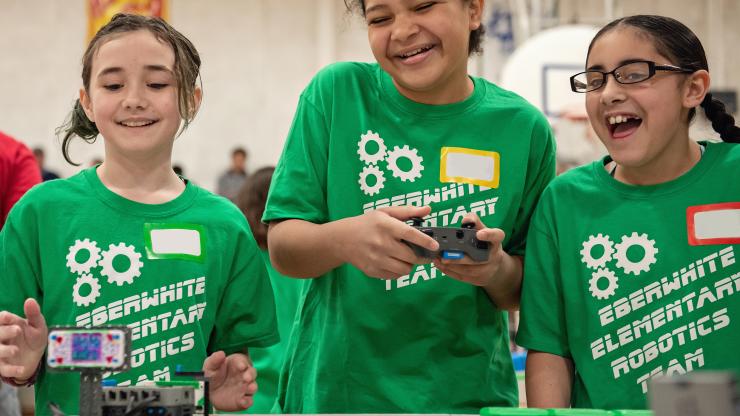 Three young students happily test robotics.