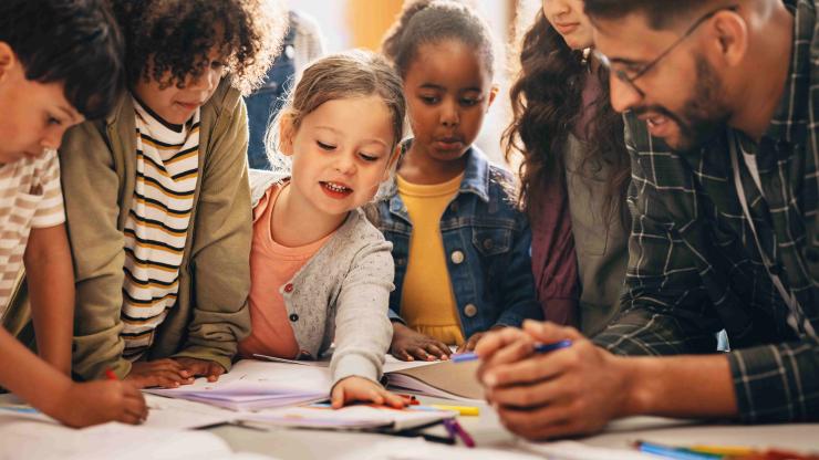 Students doing a creativity project with their teacher in a classroom. Group of primary school children learning how to draw and colour with the help of their educator.