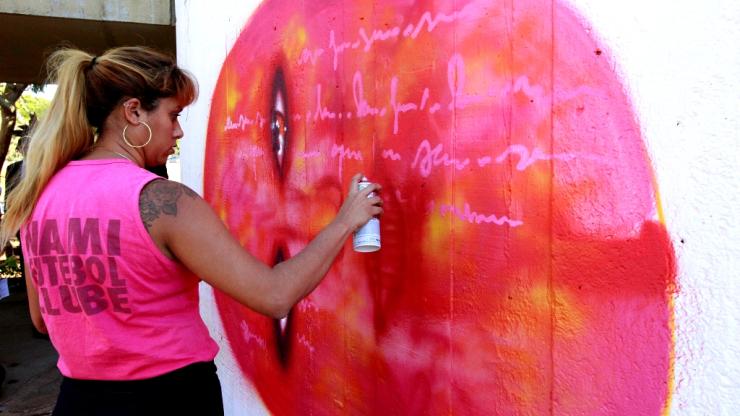 Brazilian graffiti artist Panmela Castro works on a mural project, spray painting a bright pink image.