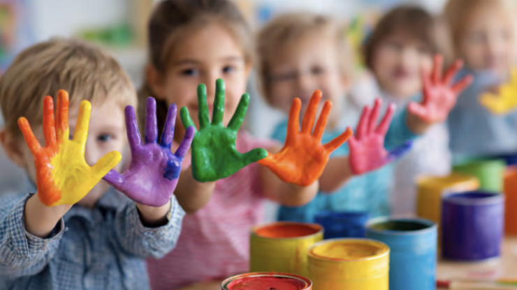 young children hold their hands out showing colorful paint on their hands