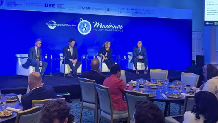 Four speakers presenting in front of a blue backdrop in a conference space 