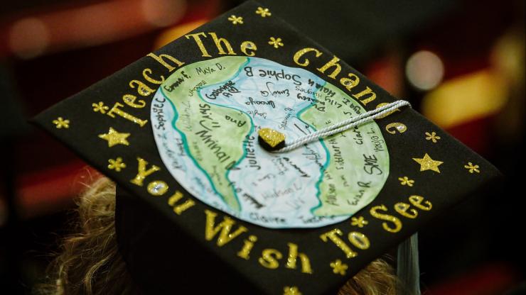 A graduate mortarboard with a hand-drawn depiction of the globe surrounded by the words "Teach the change you wish to see."