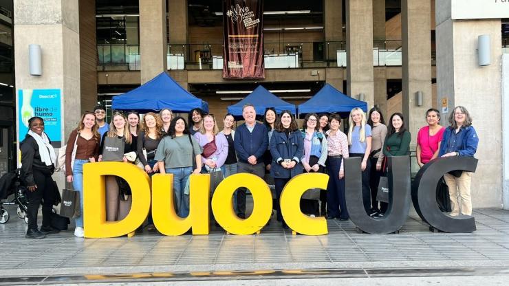 CSHPE students pose on a plaza outside a building with a large sign in front that reads "DuocUC."