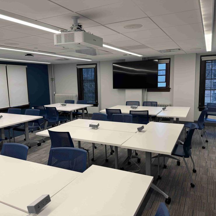 Image of classroom interior with tables, chairs, a monitor, and projector