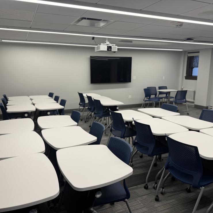 Image of classroom interior with tables, chairs, a monitor, and projector