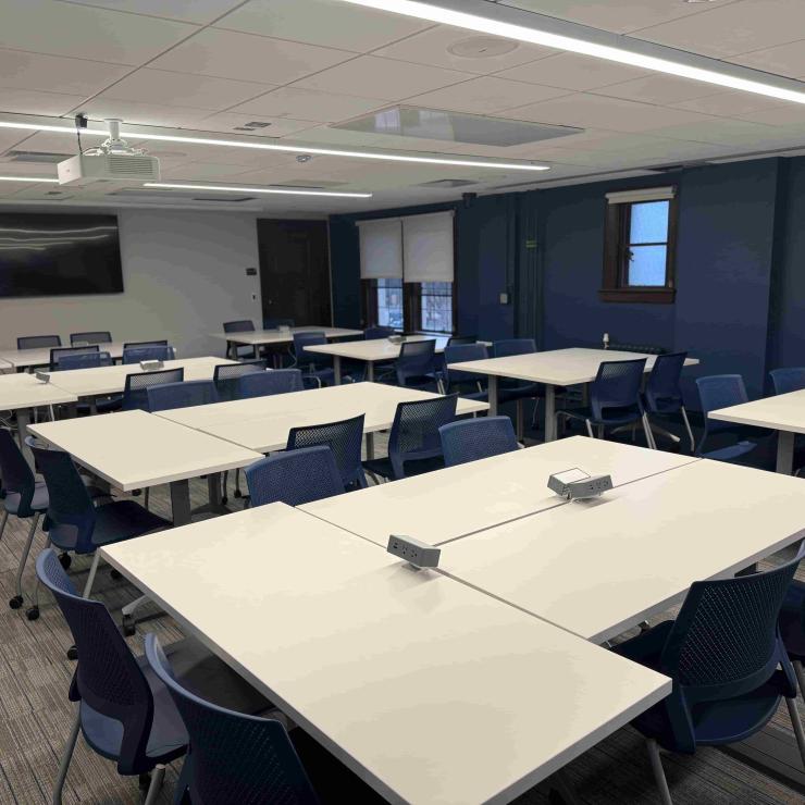 Image of classroom interior with tables, chairs, a monitor, and projector