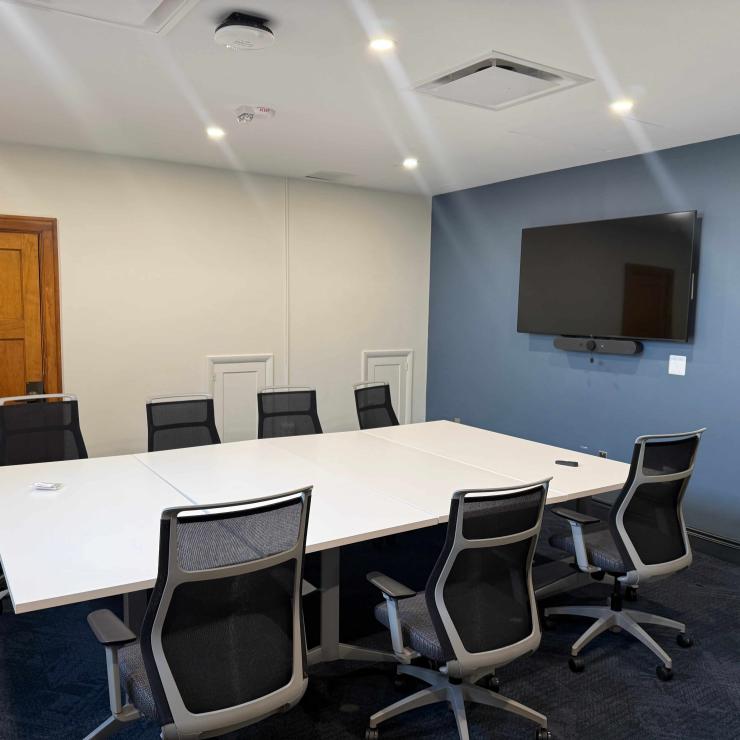 Image of conference room, with one table surrounded by chairs, and a monitor on the wall