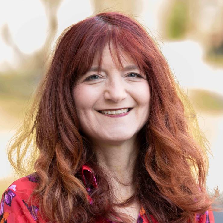 Image of smiling woman with shoulder length red hair, wearing a red blouse