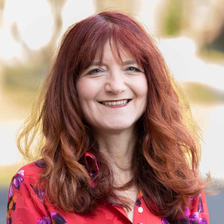 Image of smiling woman with shoulder length red hair, wearing a red blouse