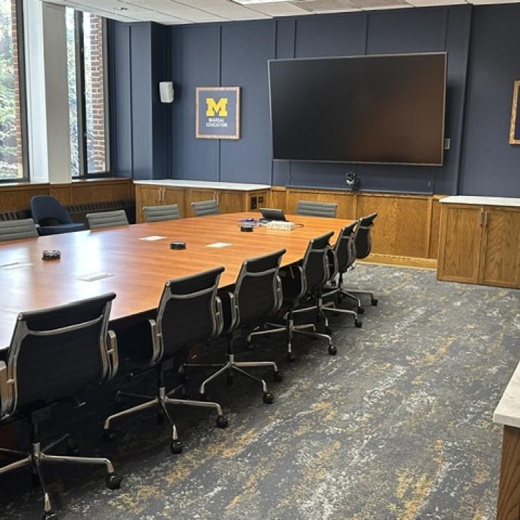 A conference desk with chairs, a monitor and block M's on the wall