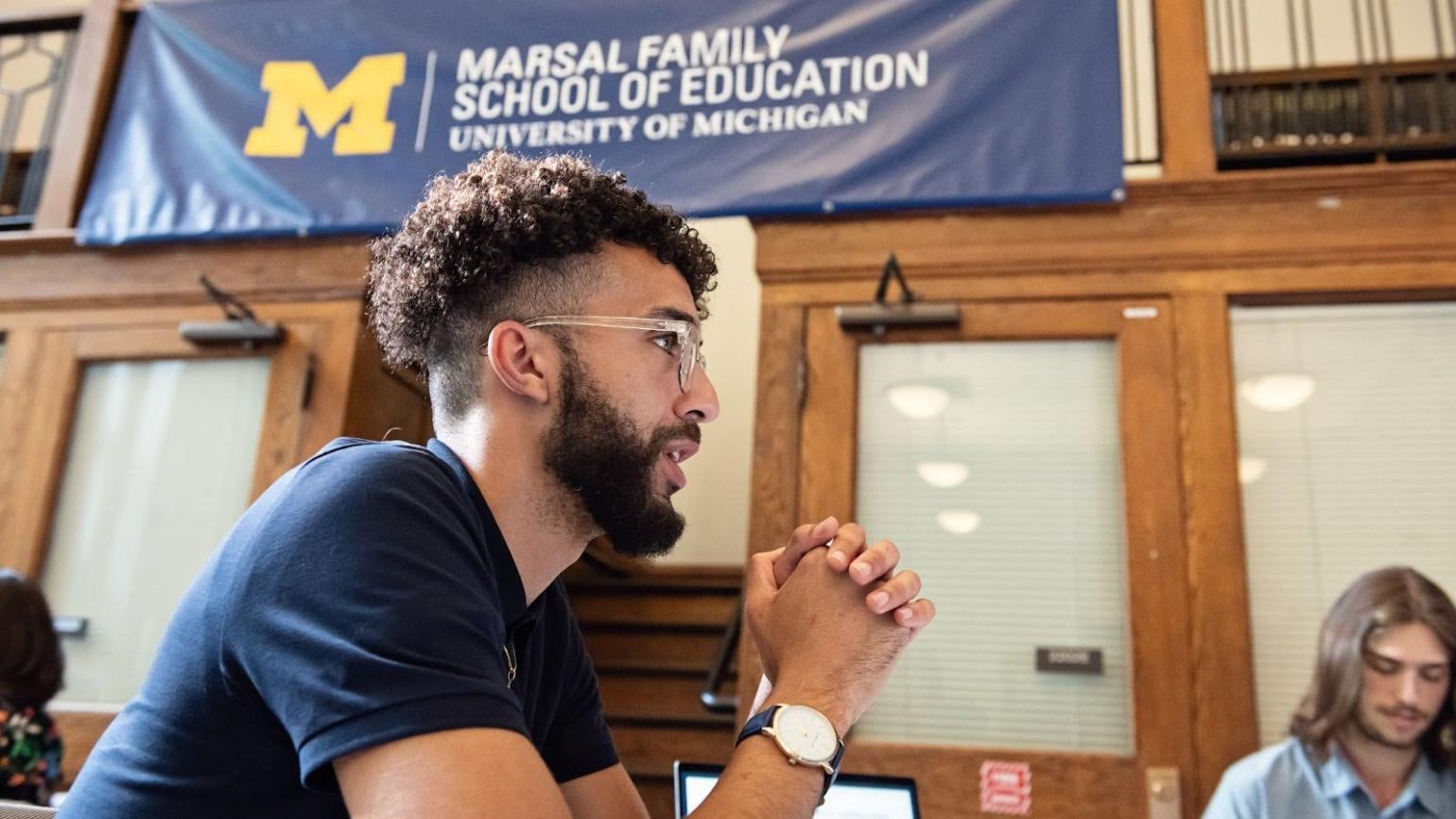 A person sits beneath a Marsal Family School of Education banner