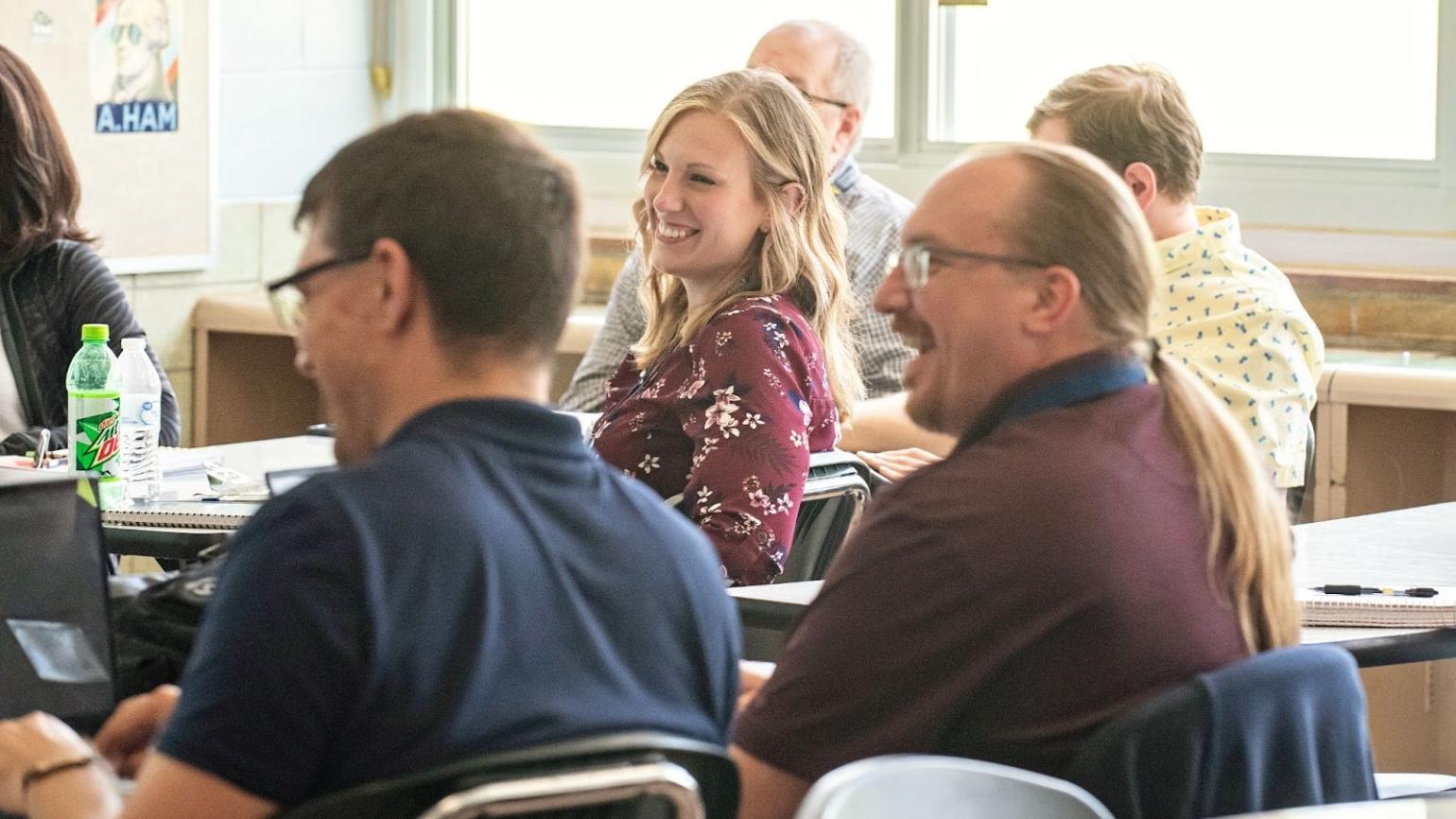 A group of adult students in a classroom share a laugh.